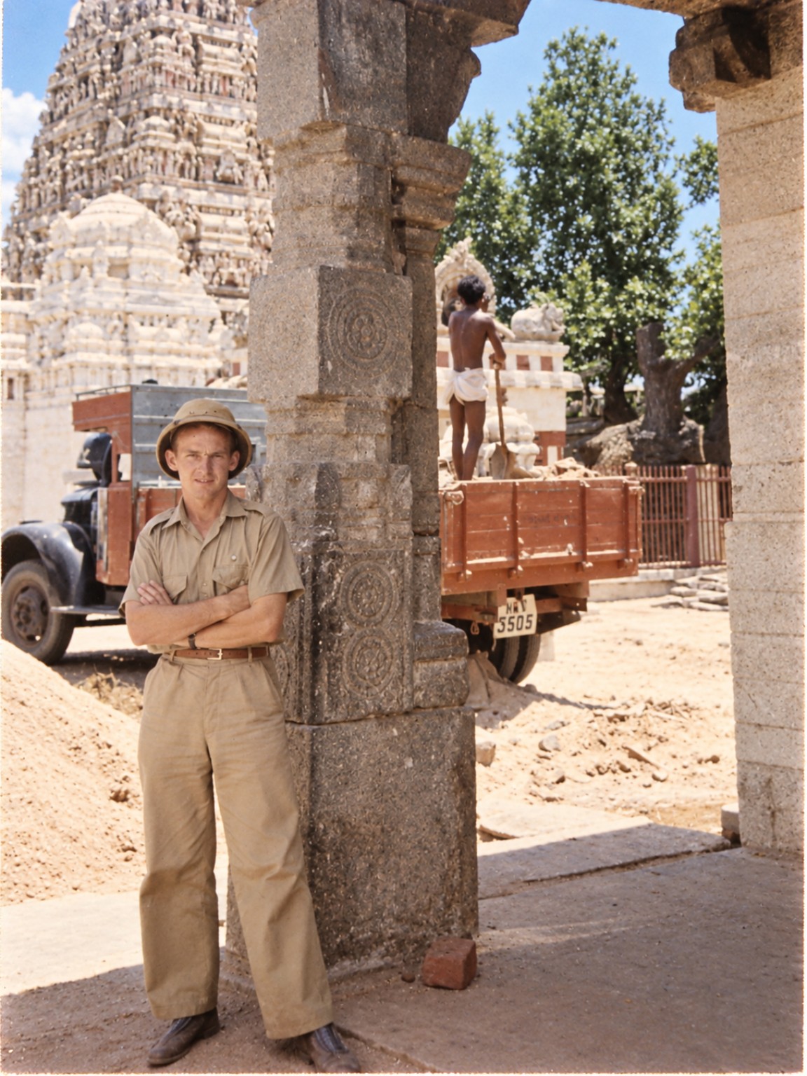 Restored family photograph of Roy Pelling in tropical clothing and a sun helmet beside carved stone pillars and a temple tower.
